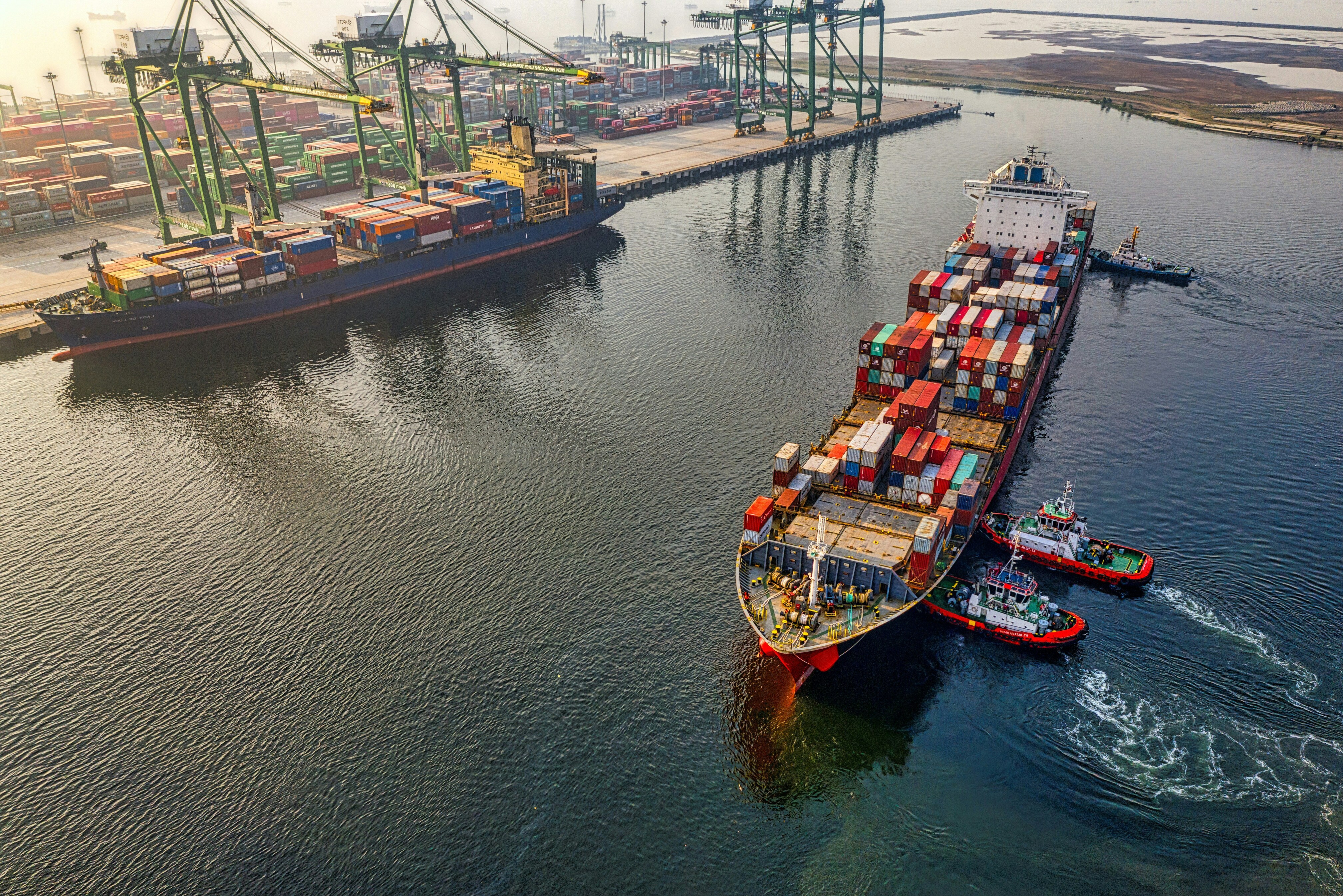 Large cargo ship with containers under a blue sky for EXPT.CO, with tugboats assisting.